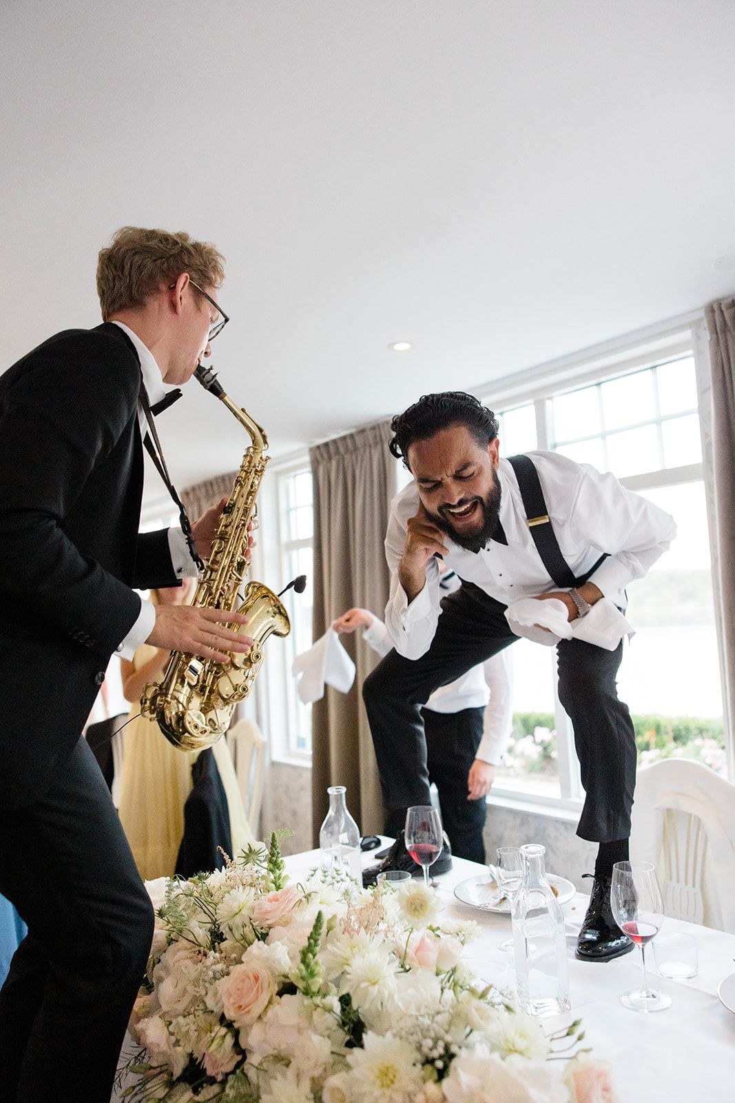 Musicians in formal attire perform energetically at an elegant wedding reception with floral centerpieces.