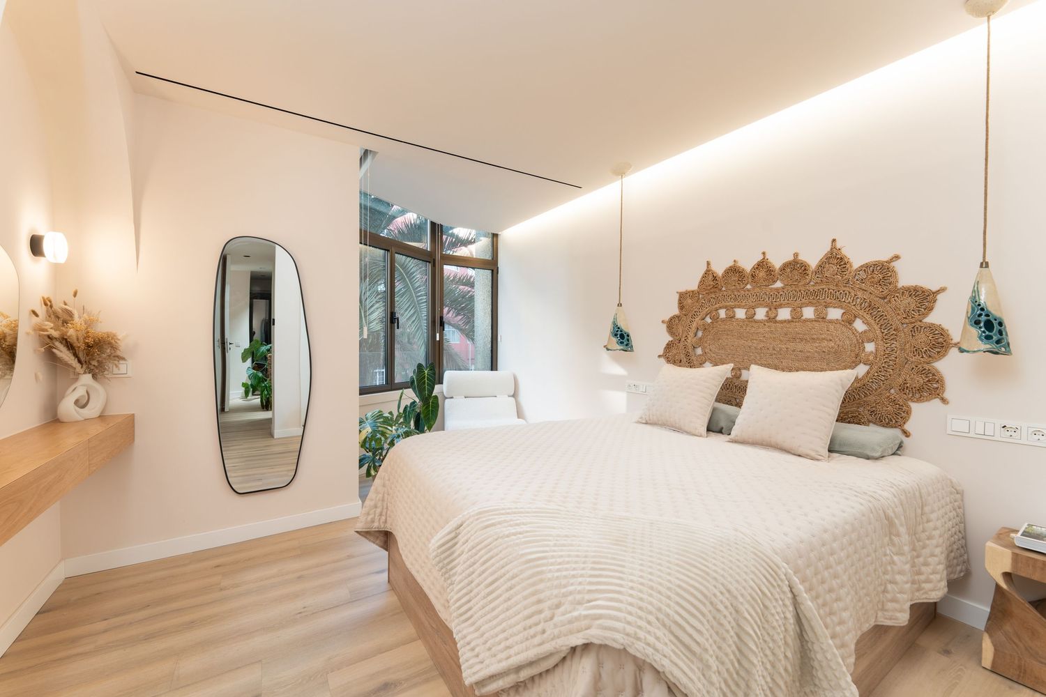 Modern bedroom interior with white bedding, wooden accents, and natural light streaming through vertical windows.
