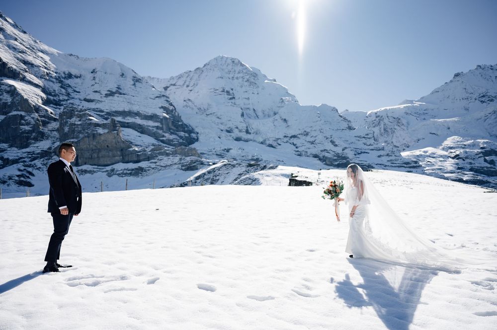 A winter wedding photo shoot against snowy Swiss Alps mountains with bright sunlight in Kleine Scheidegg, Switzerland.