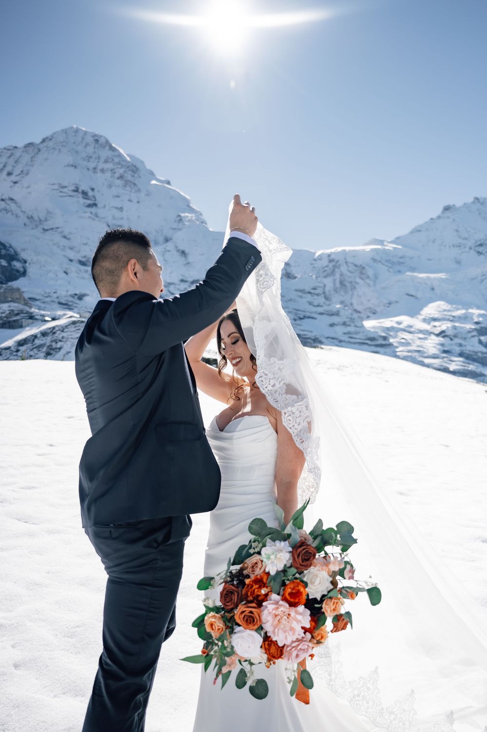 A wedding couple shares intimate moments in a snowy mountain landscape with snow-capped peaks in the background.