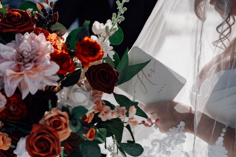 A romantic floral arrangement featuring deep red roses, pink blooms and greenery against a white backdrop.