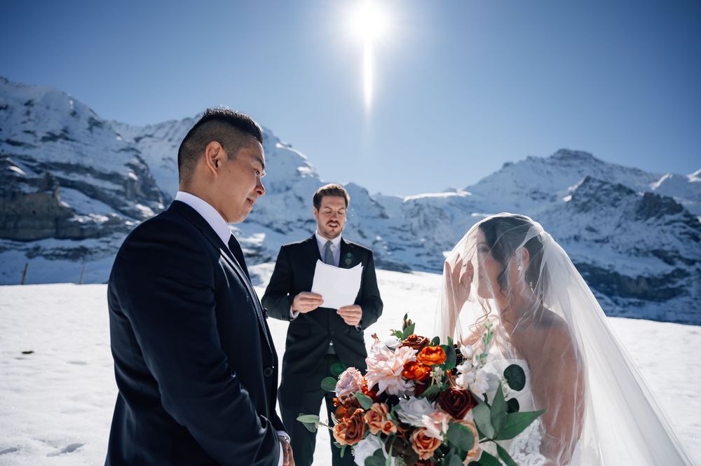A winter wedding ceremony takes place against a backdrop of snow-covered mountains in the Swiss Alps.