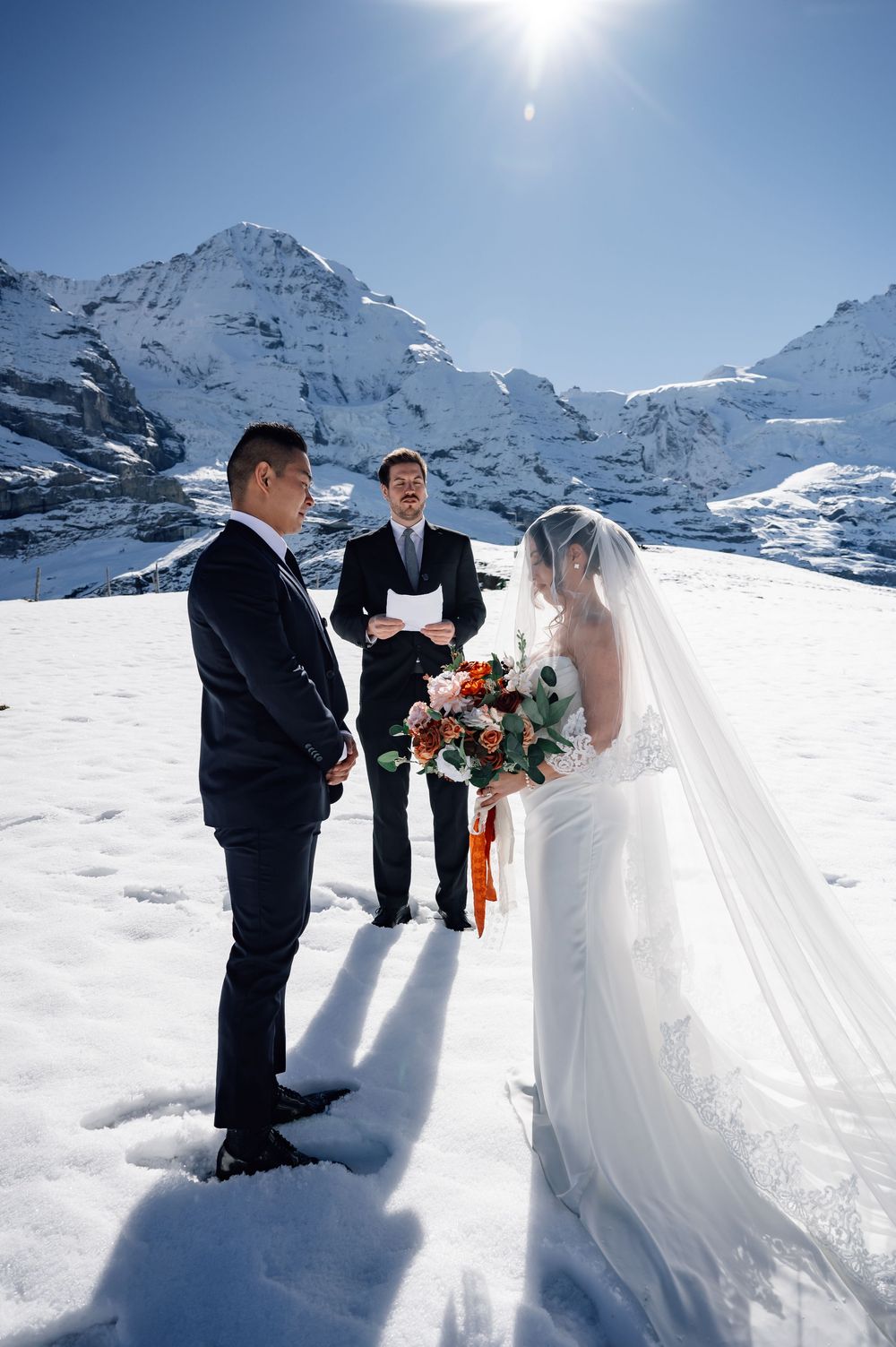 A winter wedding ceremony takes place against a stunning backdrop of snow-covered mountains in the Swiss Alps.