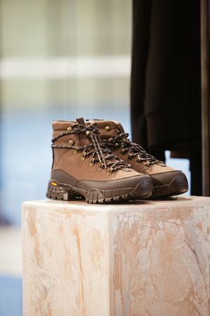 Brown leather hiking boots with green laces displayed on a marble pedestal in a retail setting.