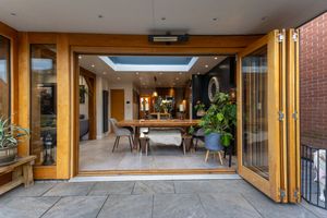 Modern dining room with bi-fold doors opening to patio, featuring wood accents and natural lighting from skylight.