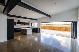 A sleek modern room with polished concrete floors and exposed ceiling beams reflects light from large windows.