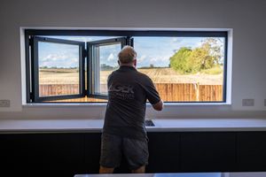 Long horizontal window frames provide scenic views of the surrounding landscape and sky from inside a modern building.