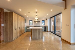 Modern luxury kitchen with marble floors, wood cabinets, and large island featuring recessed lighting and sliding glass doors.