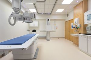 Modern medical facility interior showing multiple rooms with diagnostic imaging equipment and examination tables.