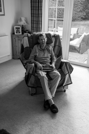 A series of black and white photos showing someone sitting and laughing in a comfortable armchair by a window.