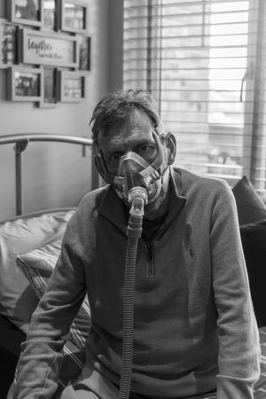 A person in a gray sweater sits on a couch while wearing an oxygen mask, shown in multiple sequential frames.