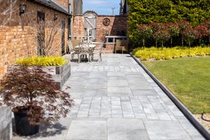 Stone walkway with curved edges leads through landscaped garden with brick walls and green lawn.