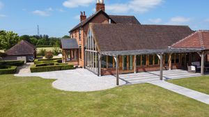 Aerial view of a modern rustic barn-style event venue with covered porch and landscaped grounds on a sunny day.