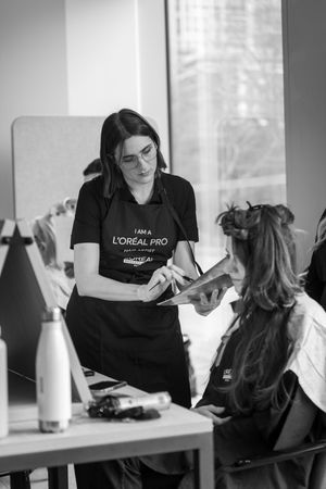 Hairstylist in black L'Oreal uniform working on client's hair at salon station with mirror and styling tools.