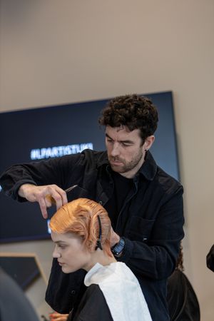 A hairstylist wearing black works on styling bright orange hair in a salon setting.
