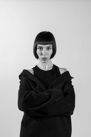 Black and white portrait of a person with short dark bob haircut wearing a black sweater against light background.