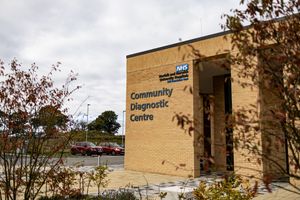 A tan brick community diagnostic center building with signage and autumn trees in the surrounding landscape.