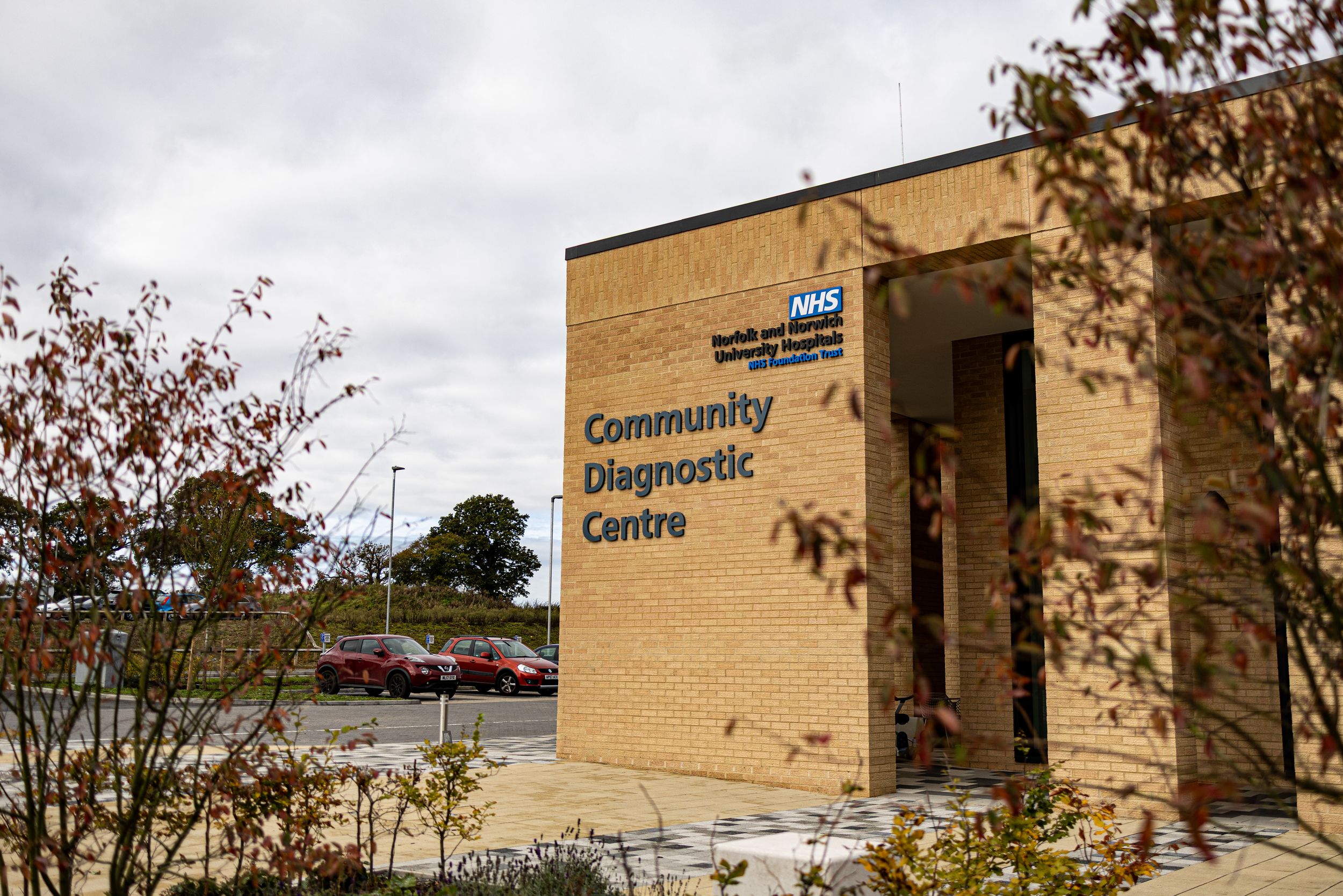 A tan brick community diagnostic center building with signage and autumn trees in the surrounding landscape.