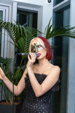 Woman in black sequined dress laughs while holding up a drink against a modern interior with tropical plants.