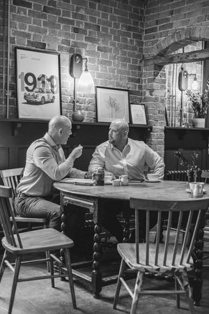 Two people sit at a wooden table in a rustic restaurant with exposed brick walls and framed artwork.