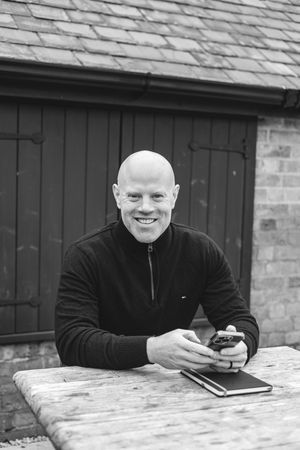 Series of black and white photos showing someone sitting at a wooden table looking at a mobile phone.