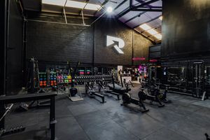 Dark industrial gym interior with black walls, fitness equipment and colorful LED lighting along the perimeter.
