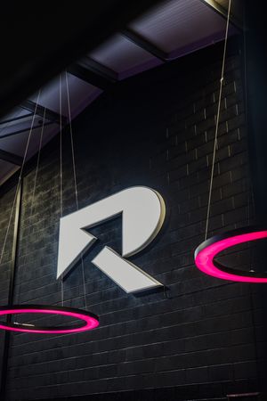 A series of black brick walls with white geometric shapes and a pink neon curve creating an abstract architectural pattern.