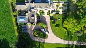 Aerial drone view of a luxury estate with swimming pool, manicured lawns and circular driveway surrounded by trees.