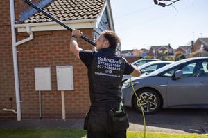Window cleaner in black uniform using a water-fed pole system to clean residential windows.