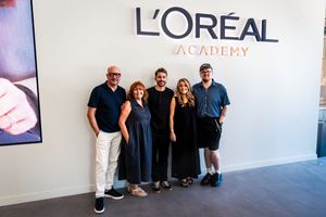 Five professionals posing together in front of the L'Oreal Academy sign in a modern studio setting.