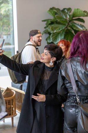 A group of people in black clothing laugh and dance together in a bright indoor space.