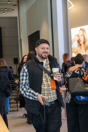 People socializing at an indoor event with someone in a plaid shirt and black vest holding a beverage.