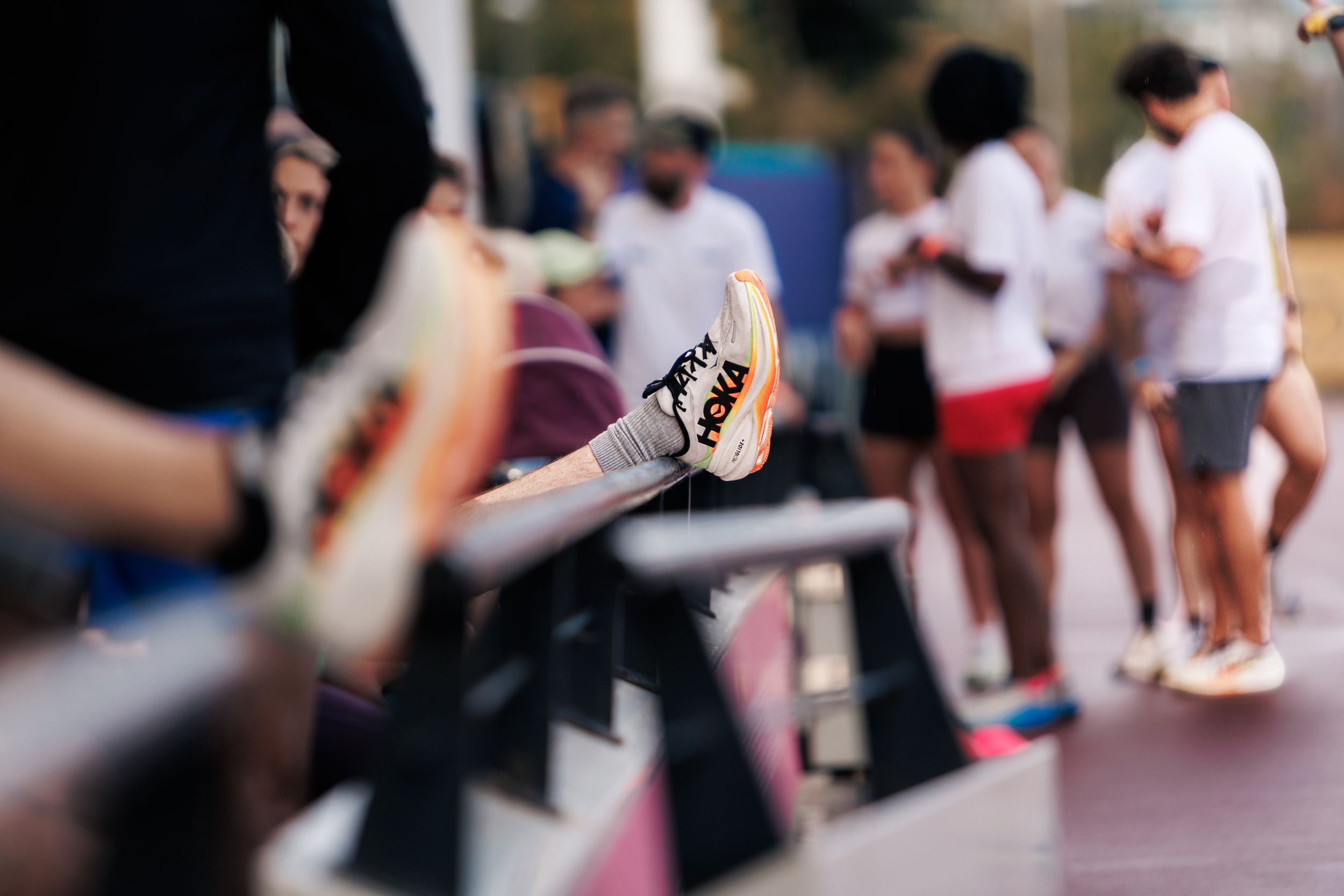 A field hockey stick held up at an outdoor sports event with players socializing in the blurred background.