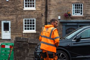 Workers in bright orange safety vests inspect a historic stone building with white-framed windows.