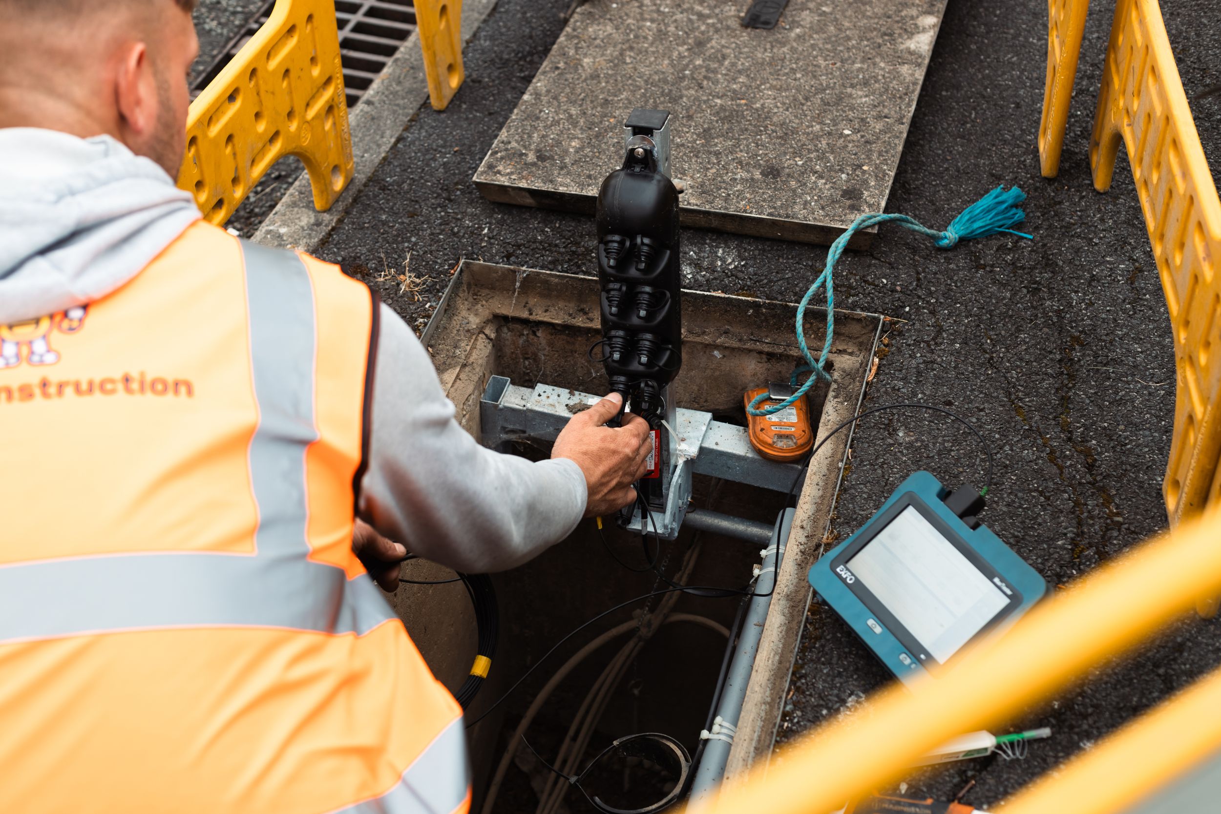 Construction worker in safety vest operates monitoring equipment in confined underground space.