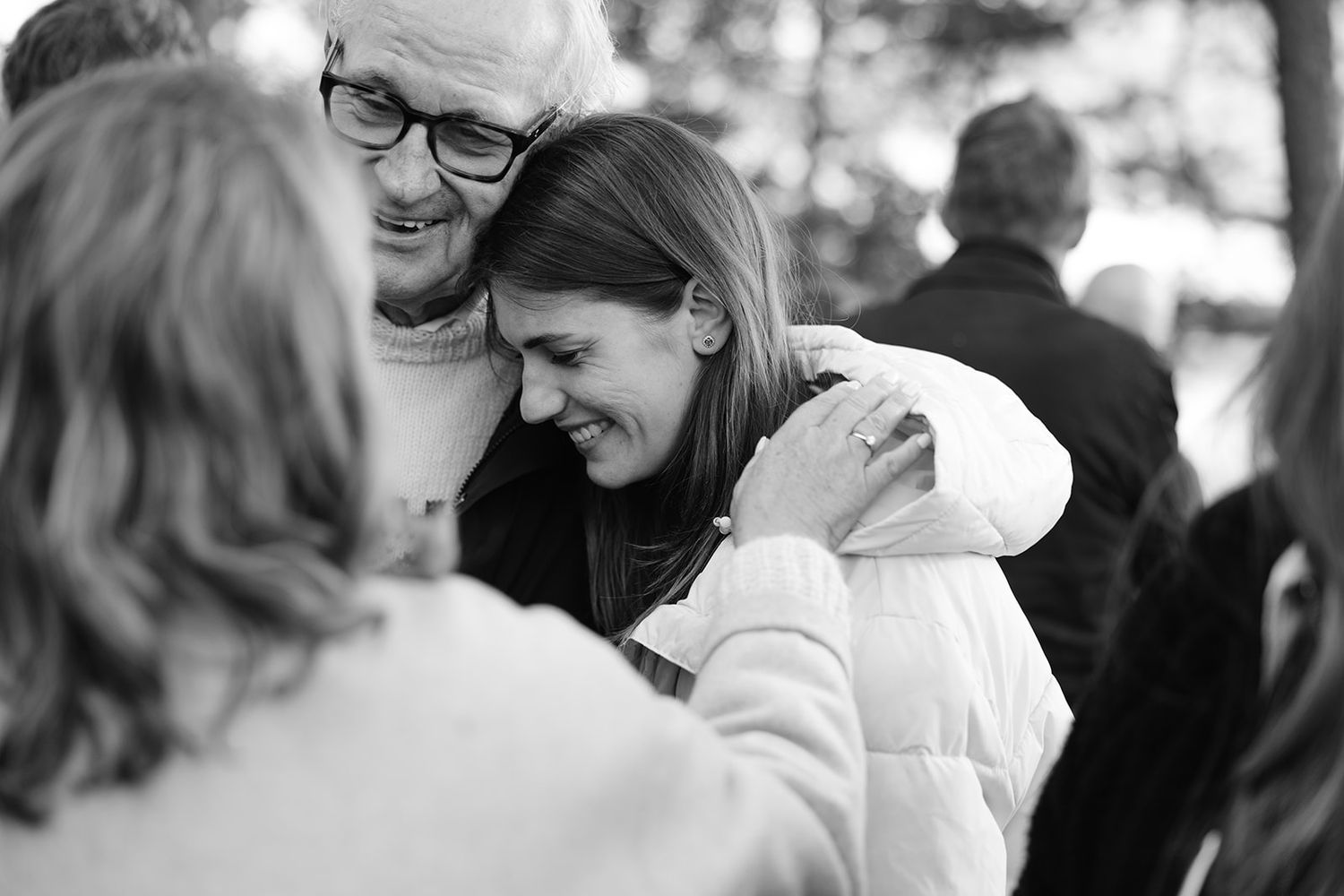 A joyful wedding celebration with guests sharing embraces and laughing together in black and white.