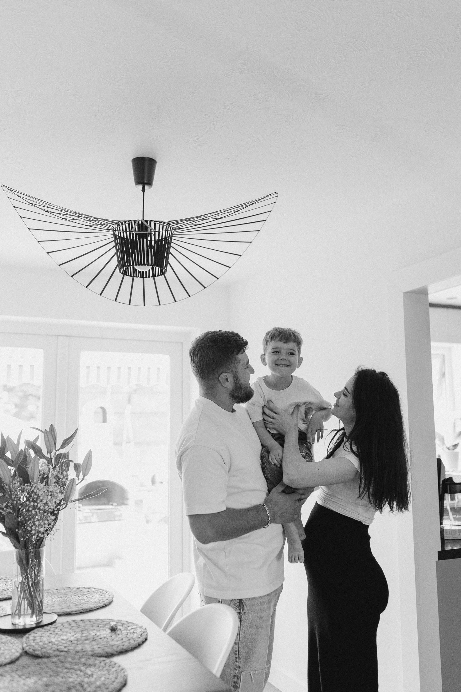 A black and white interior photo of a family moment at home under a modern sunburst pendant light fixture.