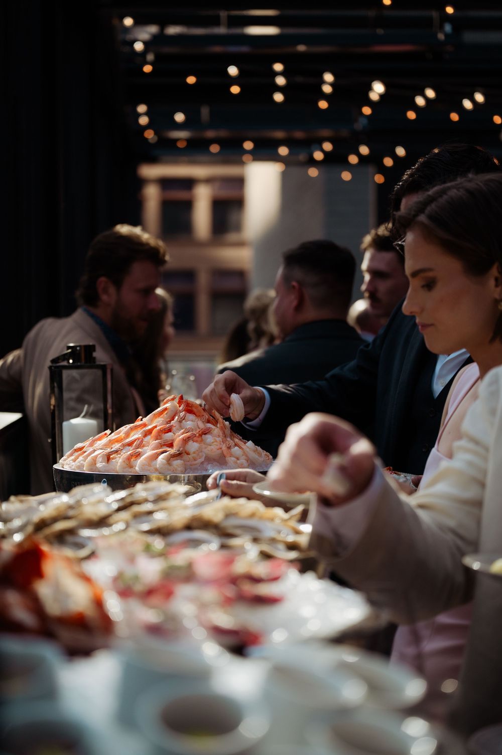 Guests enjoying a lavish seafood buffet with shrimp tower and oysters at an elegant evening event.