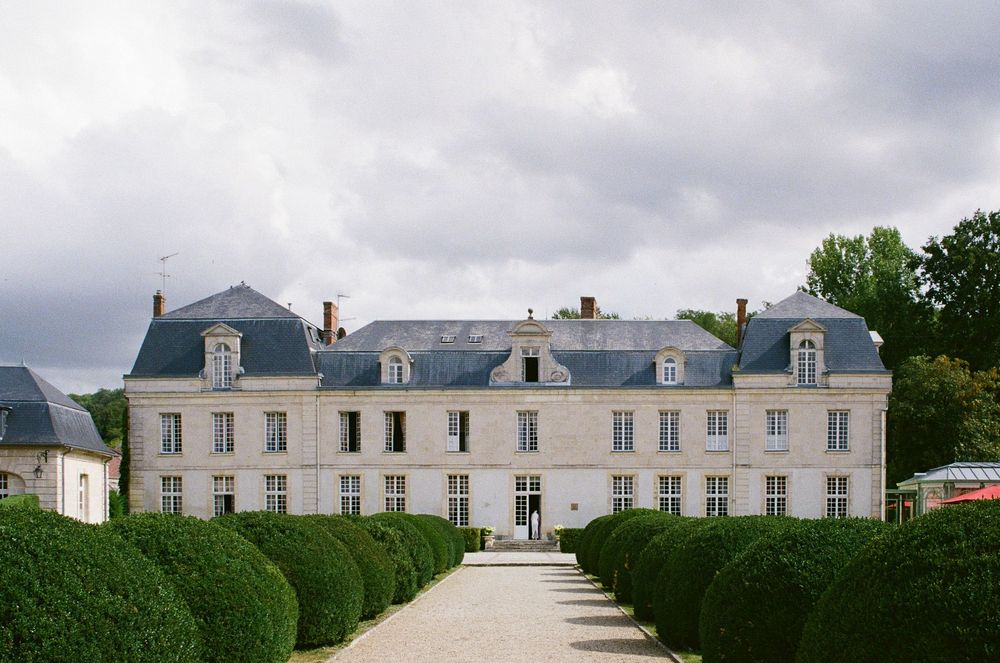 Historic white manor house with symmetrical architecture and manicured hedges stretches across a rural French landscape.