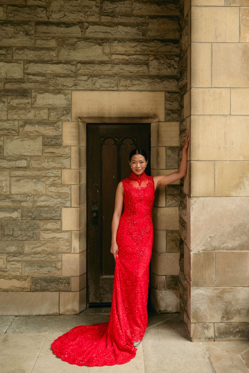 Stunning red lace dress photographed against stone architecture with dramatic lighting.