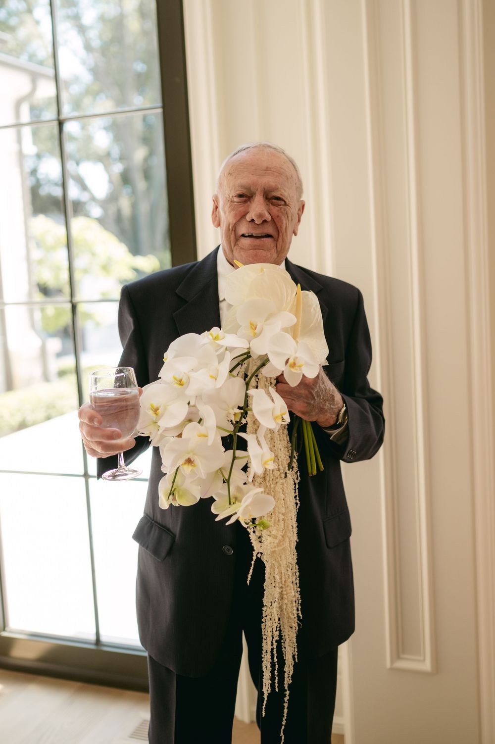 A person in a black suit holds a beautiful white orchid bouquet with cascading elements at a formal event.