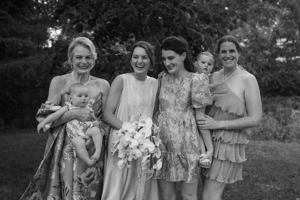 A group of people wearing floral dresses pose together outdoors in a garden setting.
