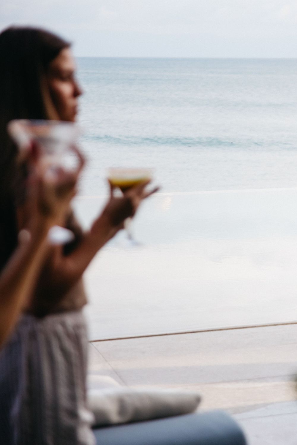 Person drinking coffee while enjoying a serene ocean view from a beachfront location on a calm day.