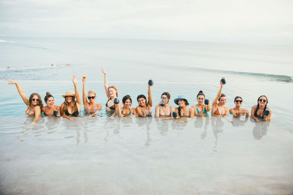 A group of friends enjoying the ocean waves together with raised arms and joyful expressions at the beach.