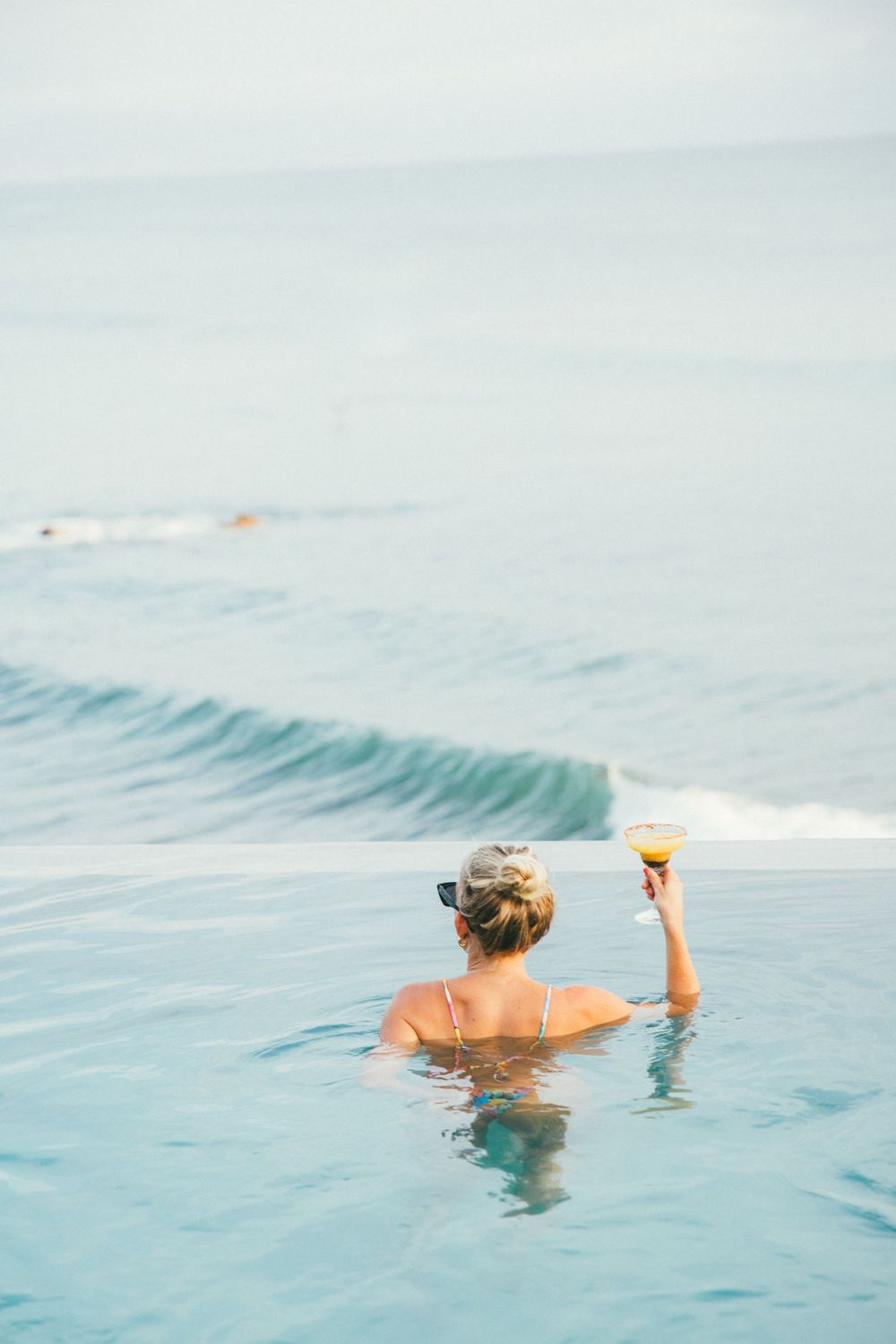 Someone relaxing in an infinity pool overlooking the ocean while holding a tropical cocktail.