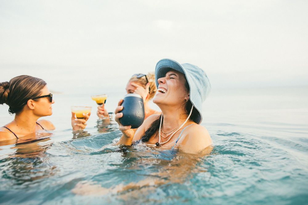 Friends enjoy refreshing drinks while floating and relaxing in clear blue ocean water on a sunny day.