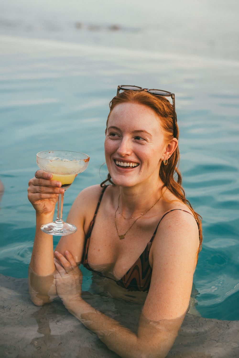 Person enjoying a margarita while relaxing in an infinity pool with ocean views.