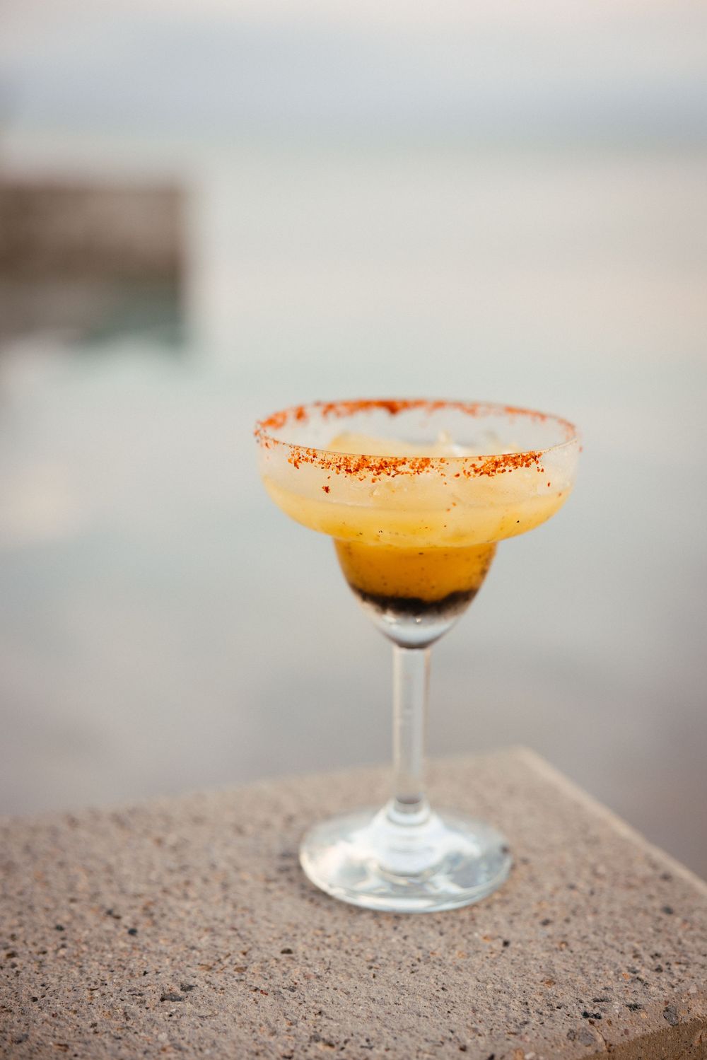 Four identical orange-hued cocktails with sugar-rimmed glasses sit on a textured stone surface in warm lighting.