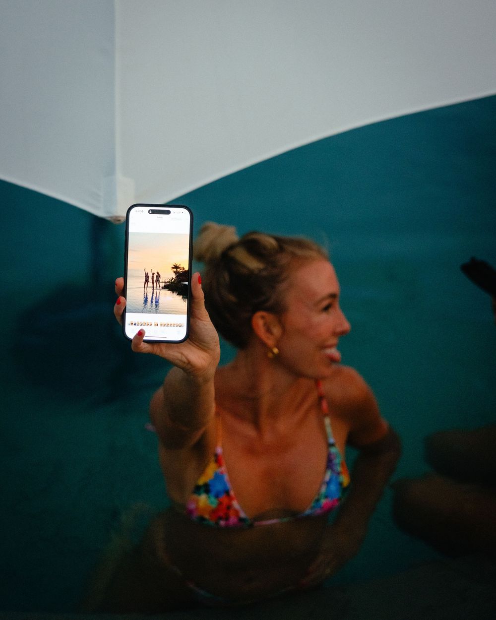 Person in swimwear holding up phone to take photo in stylish teal-walled space.