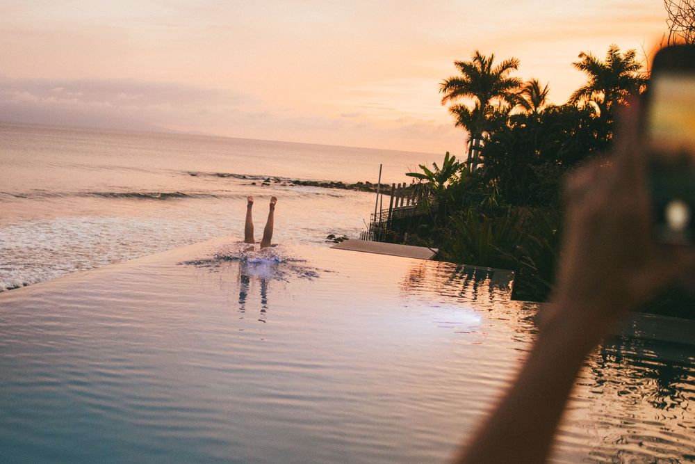 A scenic tropical beach at sunset with palm trees silhouetted against an orange sky and calm ocean waters.